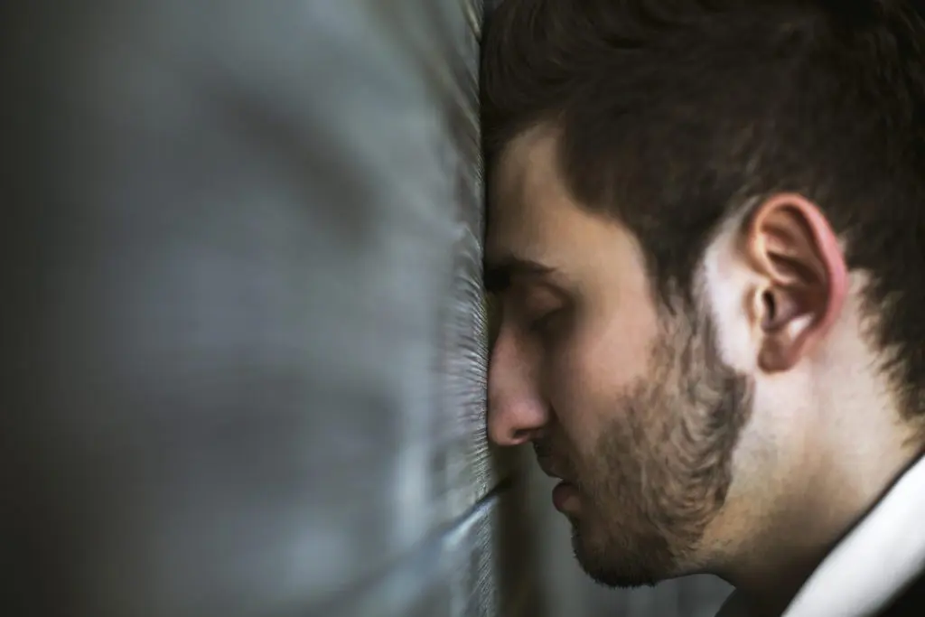 Distressed male CEO in a suit with his head pressed against a wall, representing frustration, burnout, and profit loss.