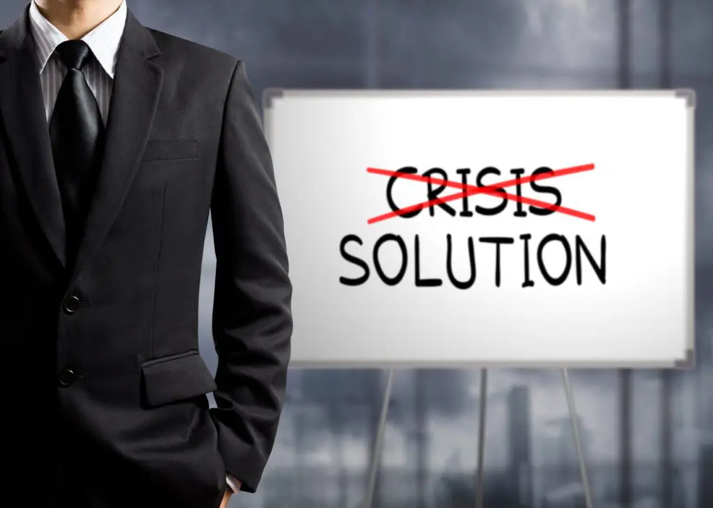 Businessman in a suit standing beside a board with the word “crisis” crossed out and the word “solution” highlighted, illustrating Step 6 of business growth strategies for CEOs.